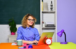 nauczycielka przy biurku z laptopem i budzikiem