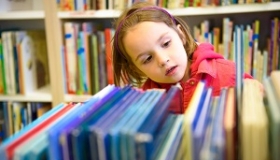 zaciekawiona dziewczynka wybiera ksiazki w bibliotece